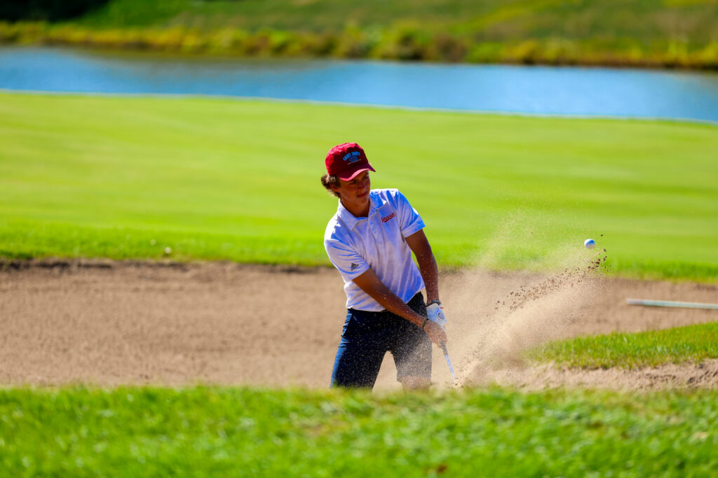 St. John's golfer swinging at golf ball in sand bunker.