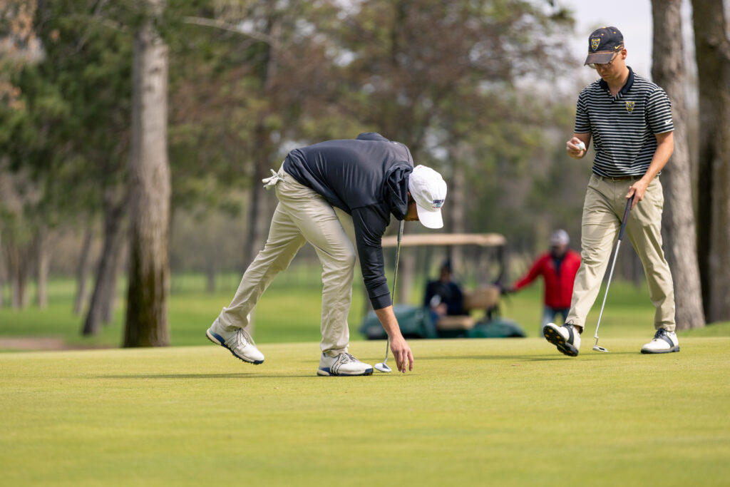 St. John's golfer bending down to grab golf ball on the tree.