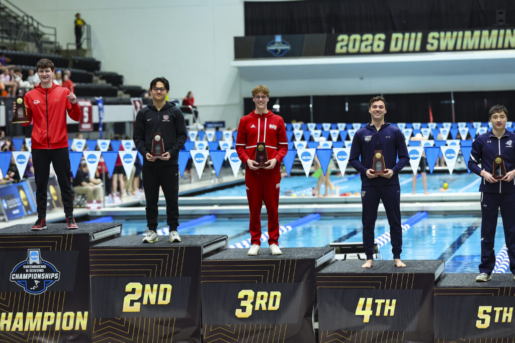 St. John's swimmer standing on podium holding All-American trophy.