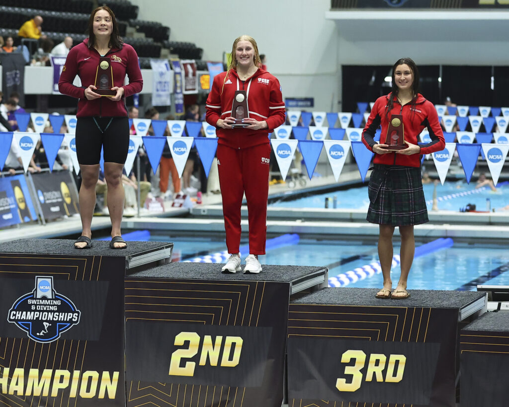 St. Ben's swimmer standing on podium holding All-American trophy.